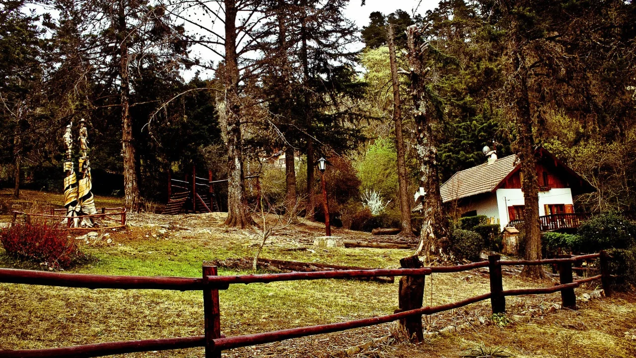 Cabaña de techo a dos aguas entre pinos, con cerco de madera, en La Cumbrecita