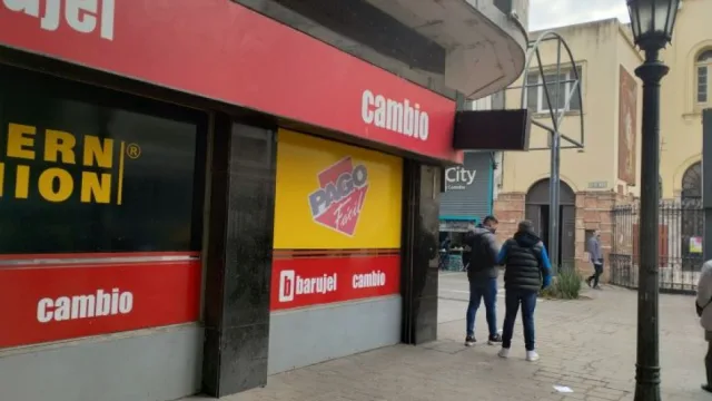 Fachada de una casa de cambio con cartel rojo y negro que incluye la palabra 'cambio' y publicidad de Pago Fácil