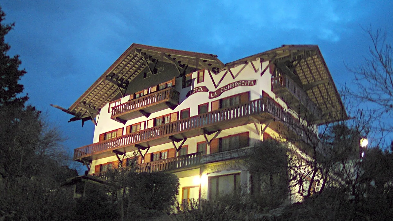Edificio de estilo alpino con balcones de madera iluminado al anochecer en La Cumbrecita