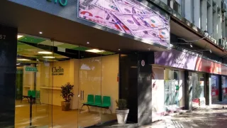 Entrada con puertas de vidrio y ventanales de entidad de cambio de divisas con cartel y sillas verdes en su interior