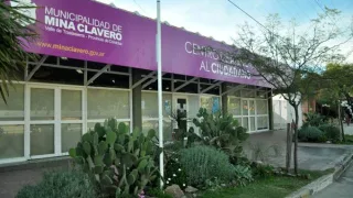 Edificio municipal con cartel morado que indica Municipalidad de Mina Clavero y Centro Cívico con plantas y árboles en la vereda