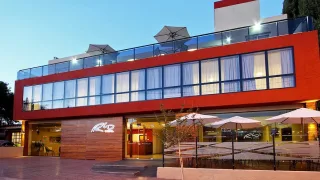 Edificio de hotel de dos plantas con grandes ventanales y terraza con sombrillas y mesas