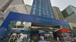 Frente del edificio del hotel Interplaza con estructura azul, cartel con el nombre hotel y alrededores con comercios