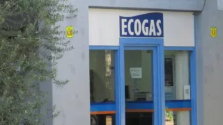 Entrada con cartel Ecogas sobre puerta de vidrio con marcos azules y pared blanca