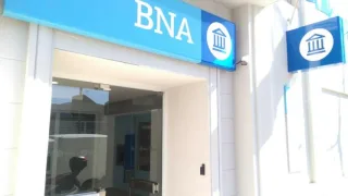 Fachada de sucursal bancaria con cartel azul y blanco de Banco Nación y símbolo de banco en puerta y pared