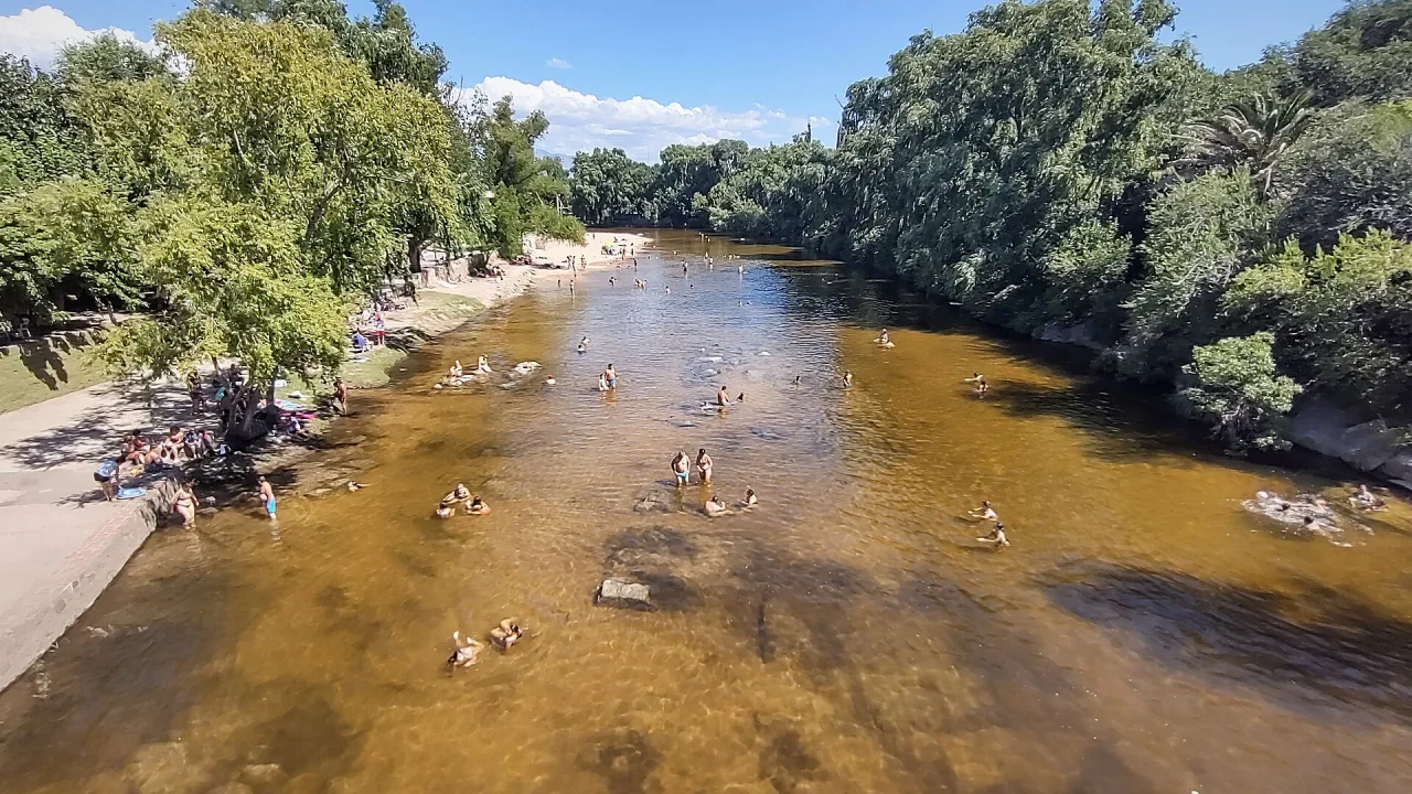 Bañistas en el río Mina Clavero, entre árboles, vistos desde el puente colgante