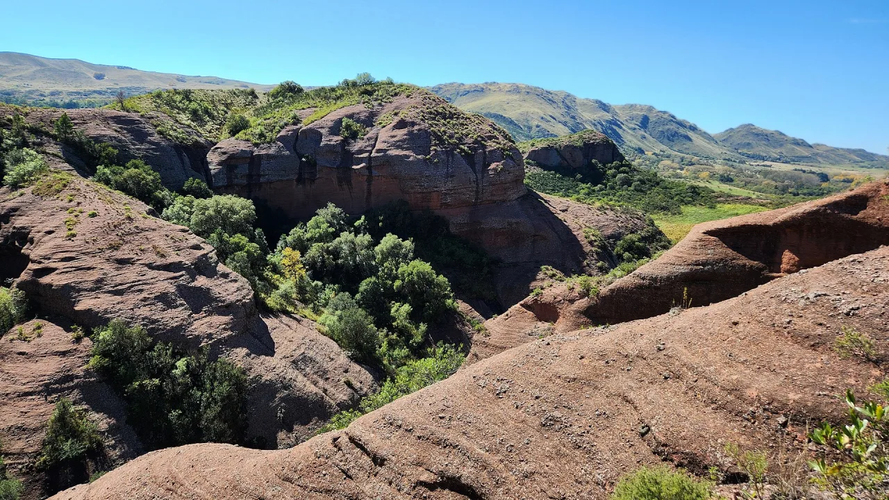 Paredones de roca rojiza y el valle de Ongamira con sierras al fondo