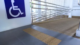Rampa con piso táctil, barandas metálicas y cartel azul con símbolo de discapacidad para facilitar el acceso a personas con movilidad reducida