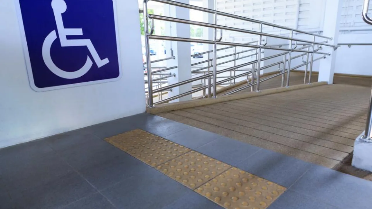 Rampa con piso táctil, barandas metálicas y cartel azul con símbolo de discapacidad para facilitar el acceso a personas con movilidad reducida