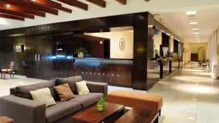Interior de la recepción de un hotel con muebles de madera oscura, sillón gris con almohadones y banco tapizado