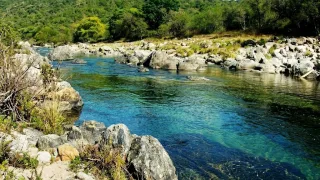 Río de agua clara y azul rodeado de rocas grandes y árboles verdes en ambas orillas