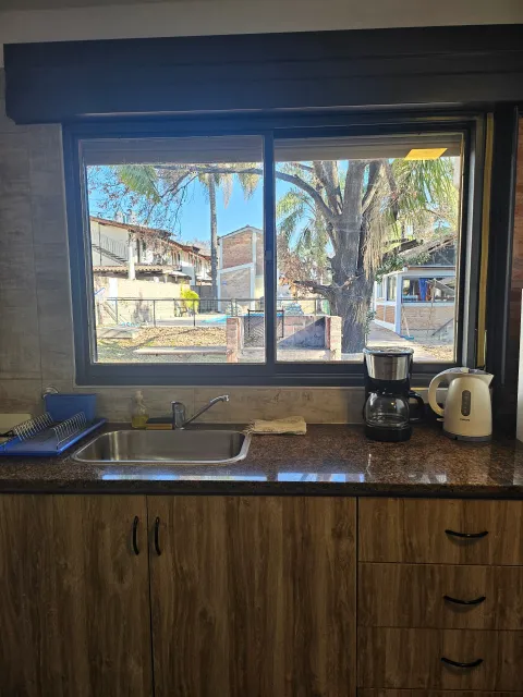 Mesada con pileta, horno eléctrico y cafetera frente a ventana que muestra patio con pileta cercada y árboles