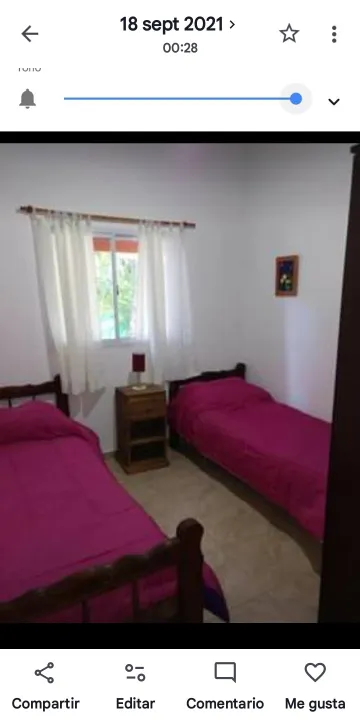 Habitación con dos camas sencillas con cubrecamas rojos, mesa de luz de madera con lámpara y ventana con cortinas blancas