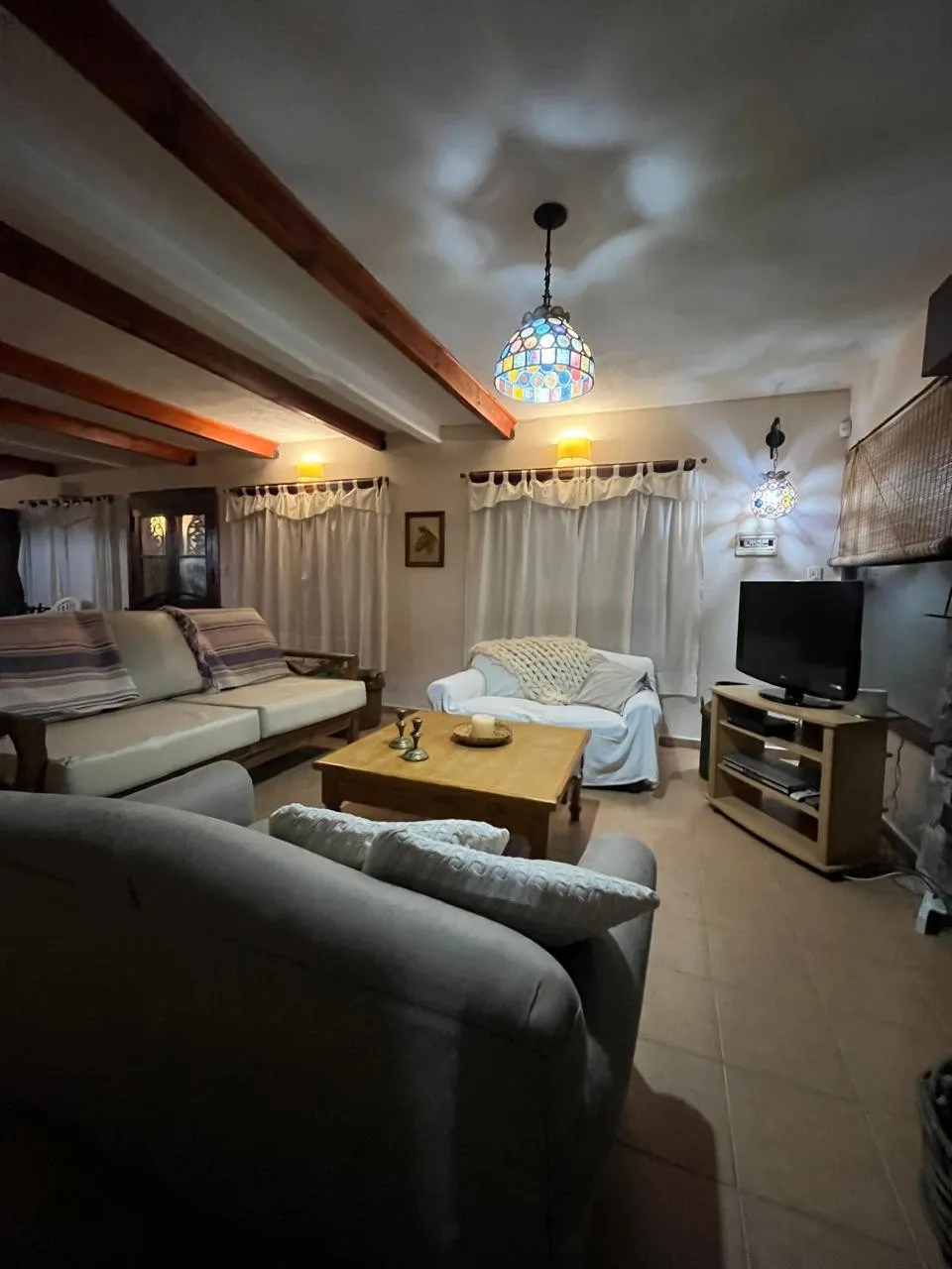 Interior de un living con tres sofás, una mesa de madera en el centro y un televisor en un mueble esquinero