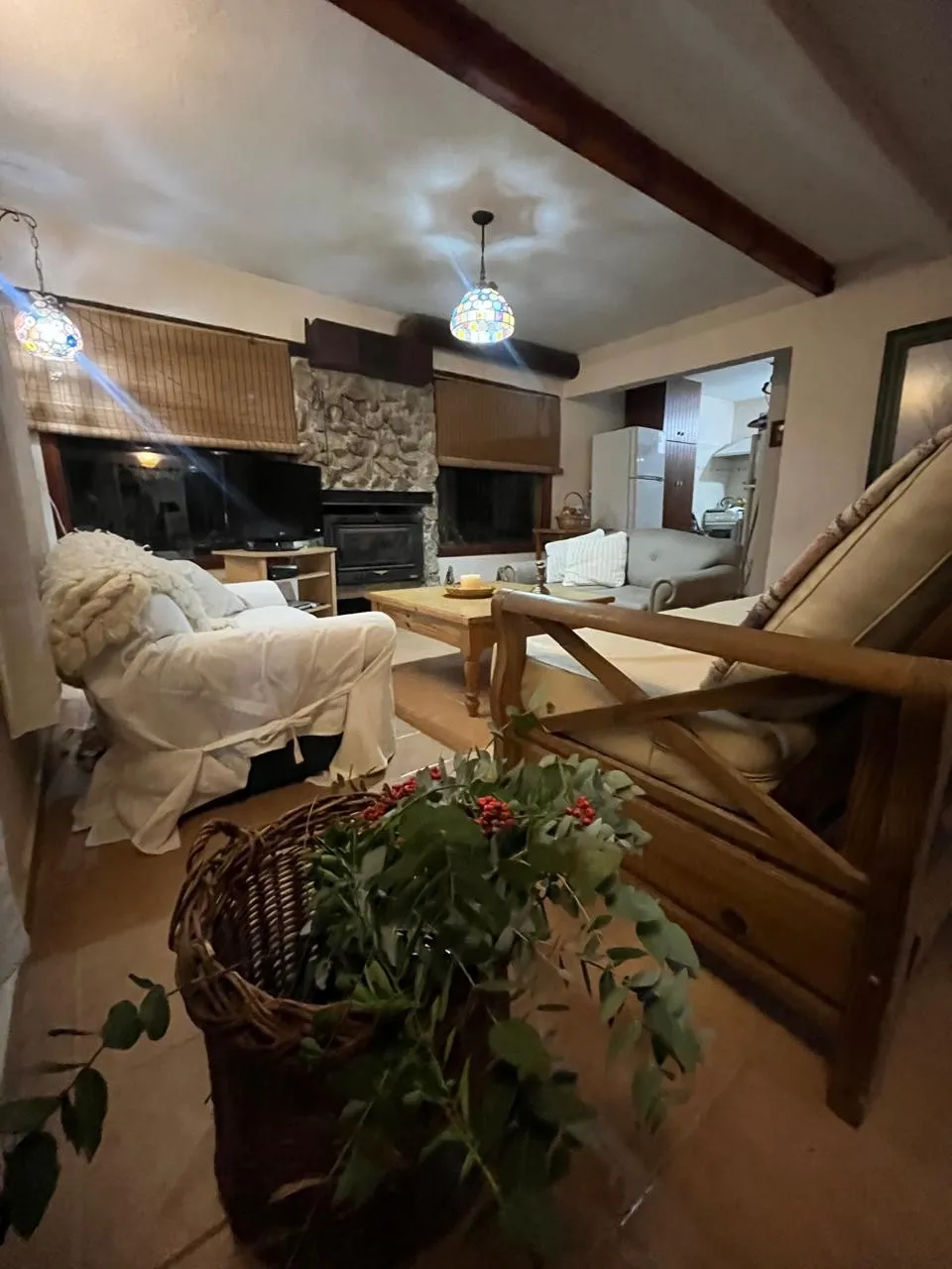 Sala de estar con sillones cubiertos con fundas blancas, mesa ratona de madera, chimenea con revestimiento de piedra y decoración con plantas y objetos rústicos