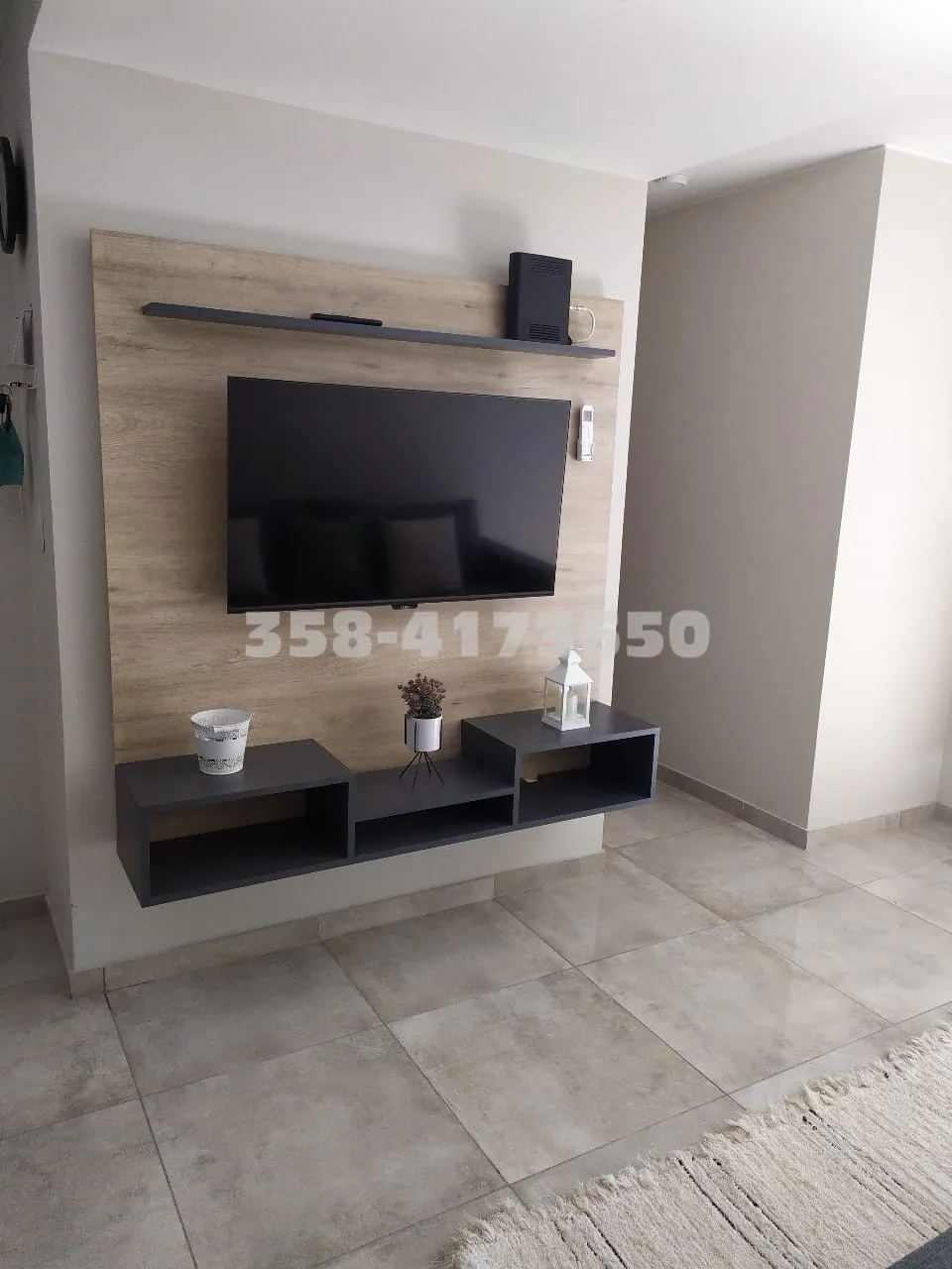 Televisor de pantalla plana colgado en pared de madera clara con mueble flotante negro y tres objetos decorativos sobre el mueble