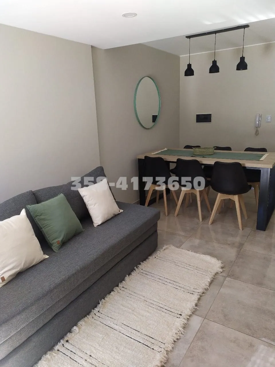 Living con sofá gris con almohadones y comedor con mesa rectangular y sillas negras en piso de porcelanato