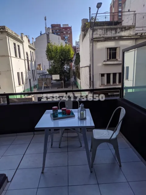 Balcón exterior con una mesa blanca y sillas y banquetas paara 6 personas