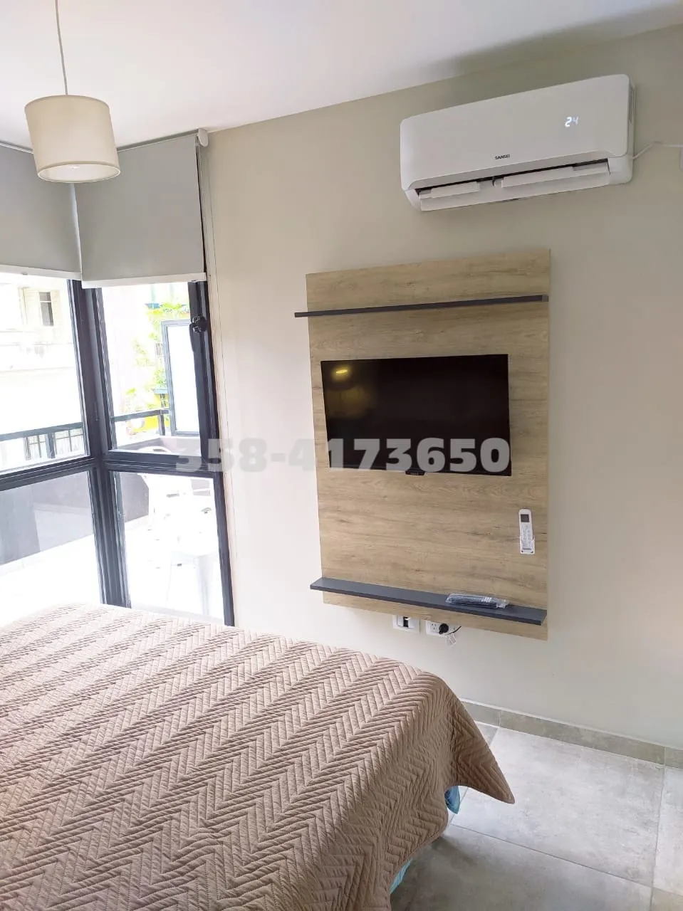 Televisión plana montada en panel de madera clara sobre la pared, ventana amplia con marco negro y puerta vidriada que da a balcón