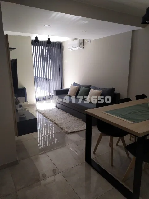 Living comedor con sillón gris con almohadones, alfombra clara y mesa con mantel azul, con luz natural que entra por ventanal con cortinas negras verticales