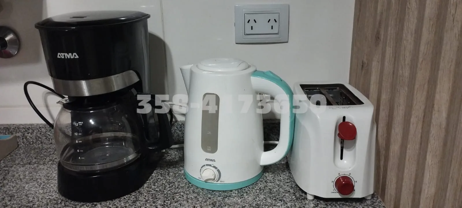 Cafetera negra, pava eléctrica blanca con detalles celestes y tostadora blanca con controles rojos sobre mesada de granito