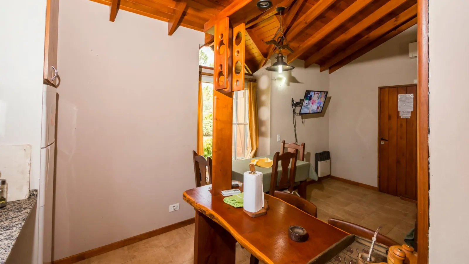Ambiente interior con comedor, mesa con sillas, barra de madera, techo de madera y ventana con vista exterior