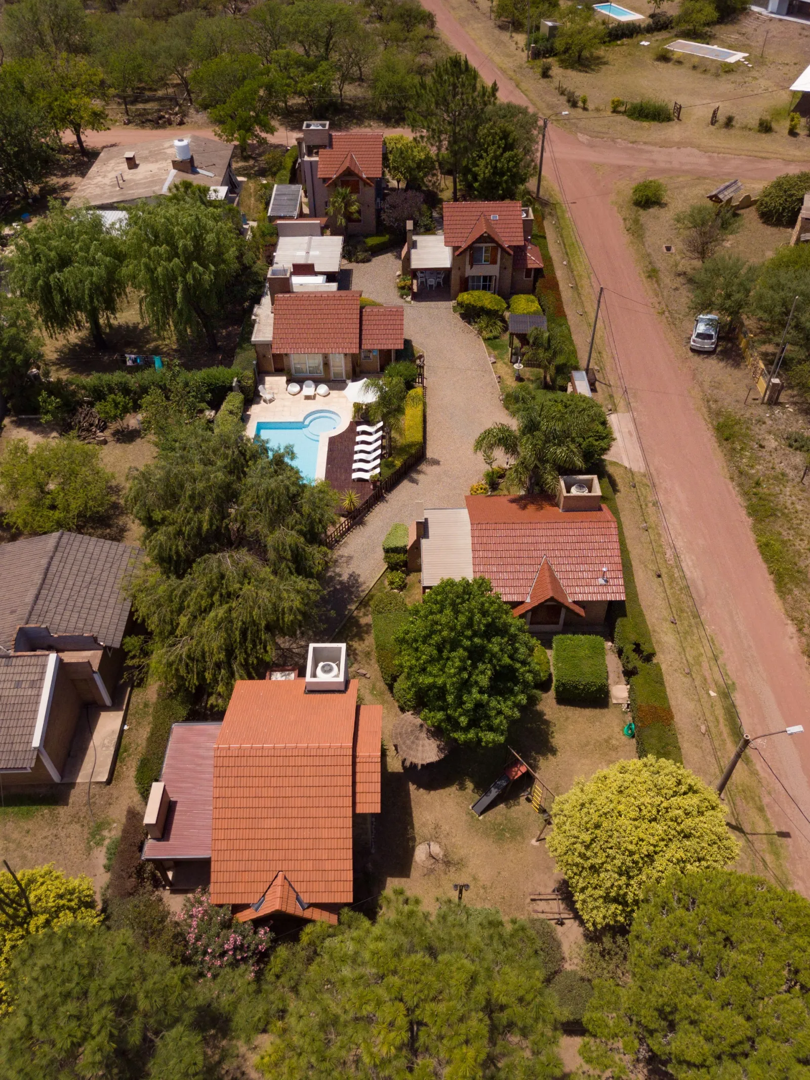 Complejo de alojamiento con varias casas, piscina con reposeras y camino de tierra