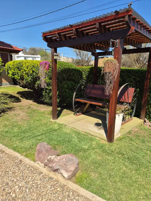 Columpio de madera con estructura de hierro negro en un espacio de jardín con césped y arbustos